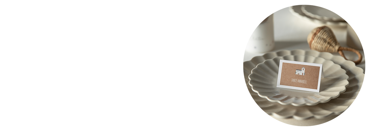 Ein Namenskärtchen, schlichtes Design, mit Text "Tante Annabell", aufgestellt auf einem Teller auf einem gedeckten Tisch